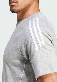 Grijze t-shirt met korte mouwen en een ronde halslijn, voorzien van drie witte strepen op de schouder en een zachte, gestructureerde stof.