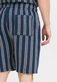 Marineblå shorts med hvide lodrette striber, med en lomme på siden og et tekstureret stof. Elastisk talje for komfort.