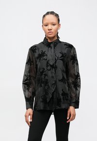 Čierna priehľadná košeľa na gombíky s kvetinovou výšivkou, dlhými rukávmi, golierom a predným zaväzovaním. Hladká textúra s priesvitným vzhľadom.