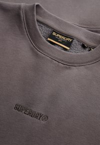 Szary sweatshirt z żeberkowym dekoltem, miękką fakturą i haftowanym logo "SUPERDRY" z przodu. Wnętrze podszewkowane dla dodatkowego komfortu.