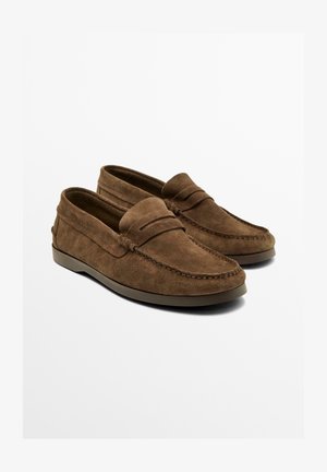Brązowe loafersy z zamszu ze szwami, noskiem w stylu mokasynów i niską, płaską gumową podeszwą, prezentowane na jednolitym białym tle.