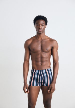 Marineblau gestreifte Badehose mit vertikalen roten und weißen Streifen, aus glattem Material gefertigt, mit Kordelzug und schmaler Passform.