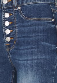 Jeans av denim i en mörk tvätt med silverfärgade metallknappar, femficksdesign och detaljer i orange söm. Slät textur och figurnära passform.