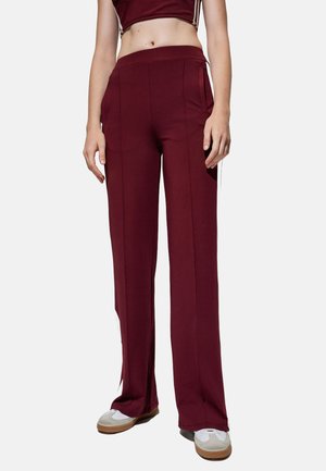 Pantalons larges bordeaux avec une texture lisse, dotés de poches latérales et de bandes blanches sur les côtés, complétés par une taille haute.