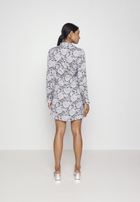 Vestido de manga longa com um padrão floral de paisley em preto e branco, apresentando uma cintura ajustada e saia rodada. Feito de tecido leve.