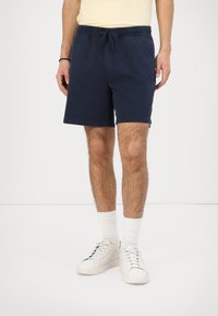 Pantaloni scurți bleumarin cu talie elastică și șnur. Construiți dintr-un material ușor, cu o textură netedă. Stilizați cu adidași și șosete albe.
