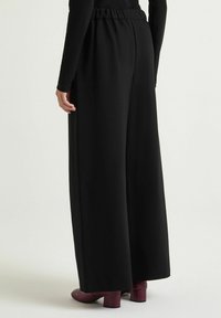 Pantaloni neri a gamba larga con vita arricciata, tessuto liscio e tasche laterali. Abbinati a tacchi bordeaux testurizzati.