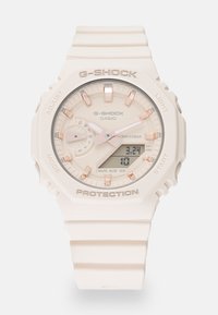 G-Shock wristwatch featuring a white silicone strap, a round cream face, rose gold accents, and analog-digital display with water resistance.