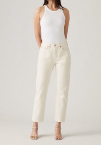 Top in cotone bianco a costine abbinato a jeans crema a vita alta e gamba dritta. Presenta leggeri sfilacciamenti agli orli e uno stile minimalista.