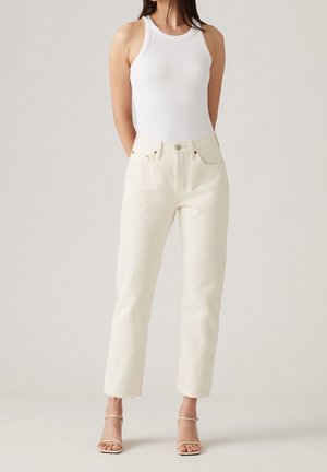 Top à bretelles blanc côtelé associé à un jean crème taille haute à jambe droite. Présente un léger effilochage au niveau des ourlets et un style minimaliste.