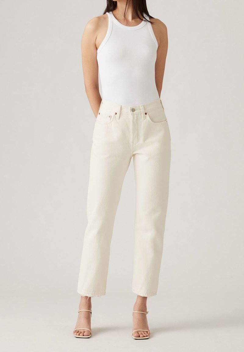 Top in cotone bianco a costine abbinato a jeans crema a vita alta e gamba dritta. Presenta leggeri sfilacciamenti agli orli e uno stile minimalista.