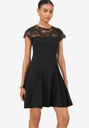 Schwarzes Kleid mit einem Oberteil aus Spitzen-Ärmeln, plissierter Rock und tailliertem Schnitt. Glattes Material mit komplizierten Spitzenakzenten am Ausschnitt.