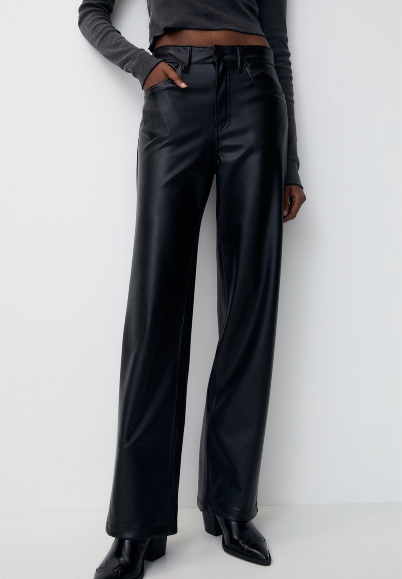 Pantalon large en similicuir noir à texture lisse, taille haute, poches avant et détails de surpiqûres contrastées.