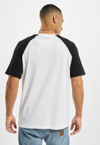 Kortärmad raglan t-shirt med vit kropp och svarta ärmar, av bomull, rund urringning och avslappnad passform.