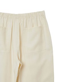 Pantaloni color crema con cintura elasticizzata, dotati di due tasche posteriori e una texture liscia e morbida. Design semplice e funzionale.