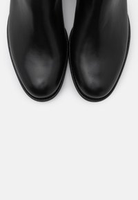 Bottines en cuir noir avec une texture lisse, un bout en amande et des coutures minimales. Les semelles sont plates et épurées.