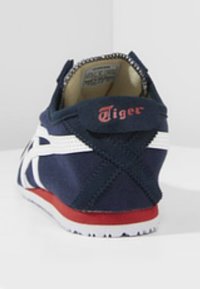 Marinblå sneaker med vita accenter, röd sula och en tigerlogotyp på baksidan. Har en texturerad tyg och en vadderad inredning.
