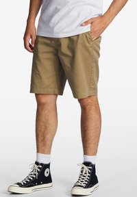 Bermuda khaki con taglio dritto e tasche posteriori, realizzati in cotone. Indossati con sneakers nere alte e una t-shirt bianca.
