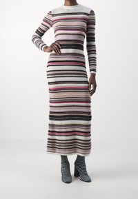 Randig stickad klänning med vertikala linjer i rosa, vitt, brunt och svart. Långa ärmar, rund halsringning och figurnära design. Svart- och vitrandiga stövlar.