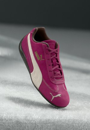 Adidași PUMA din suede fucsia cu o dunga de culoare crem pe lateral, având șireturi roz și o talpă din cauciuc negru texturat. Accente cu logo auriu.