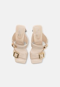 Beige vegane Sandalen mit Absatz aus Krokodilprägung, breiten Riemen und goldenen runden sowie quadratischen Schnallen am Riemen und Knöchel.