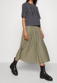Grijze cropped t-shirt met zwart "GAP" logo, gecombineerd met een geplooide olijfgroene rok en zwarte enkellaarsjes met een chunky zool.