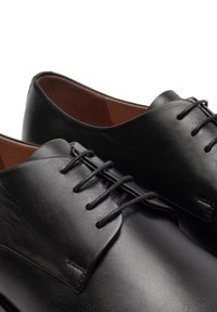 Scarpe in pelle nera con una texture liscia, punta arrotondata e chiusura con lacci. Presentano linee pulite e un design minimalista.