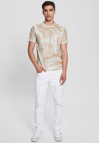 Šviesiai ruda trumpa rankovė marškinėliai su palmių lapų raštu šviesiame fone, derinami su baltais kelnėmis ir baltais sportbačiais.