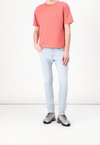 Maglietta di cotone color corallo con maniche corte, abbinata a jeans azzurri aderenti e scarpe sportive grigie con dettagli neri.