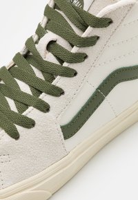 Höga sneakers i beige mocka och läder, med gröna snören, ett grönt rand och en texturerad gummisula.