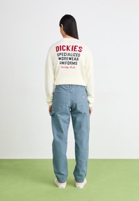White sweatshirt with red and black text on the back, paired with light blue cargo pants featuring pockets and a relaxed fit.