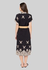 Zwarte jurk met korte mouwen en een kraag, voorzien van beige bloemenborduursel en een bijpassende stoffen riem in de taille.