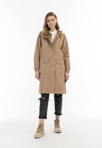 Khaki bunda s kapucí, elastickými manžetami, dvěma předními kapsami a knoflíkovým zapínáním. Nalezena přes černé roztrhané džíny a béžové šněrovací boty.