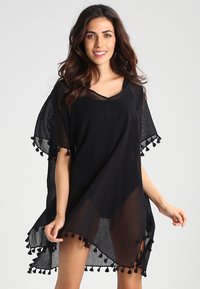 Black poncho-style cover-up made of lightweight, sheer fabric. Features tassel accents along the hem and a V-neck design.