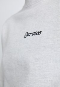Gray cotton sweatshirt featuring a round neckline and the word “Service” embroidered in black script on the chest.