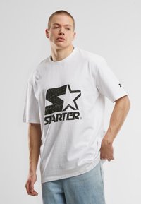 White T-shirt made of cotton, featuring a large black "Starter" logo with a star design on the front. Relaxed fit with short sleeves.