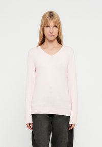 Camisola cor-de-rosa clara com decote em V, feita de material de malha suave, com mangas compridas e bainha canelada, combinada com calças escuras.