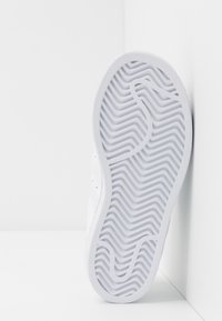 Suola di scarpa sportiva bianca con un motivo a zigzag testurizzato, caratterizzata da un bordo arrotondato e materiale in gomma liscia. Il lato mostra dettagli minimi.