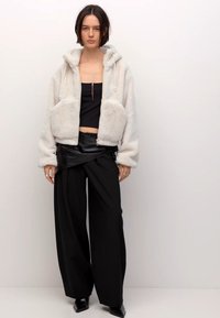 Neppere faux fur hoodie in lichtgrijs met zakken aan de voorkant, gecombineerd met een zwart cropped topje en wijde zwarte broek met een gestructureerde uitstraling.