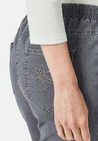 Graue Jeans mit gerafftem Bund, bestickter Gesäßtasche mit silbernen Akzenten und glatter Textur.