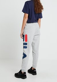 Grå sweatpants med en stor marinblå och röd grafisk design på vänster ben, ihop med en marinblå t-shirt och svarta sneakers.