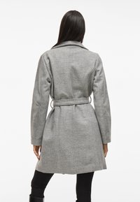 Szary wełniany płaszcz z paskiem w talii, klapami, długimi rękawami oraz teksturowanym wykończeniem. Tył ma zgrzane szwy, co nadaje mu elegancki fason.