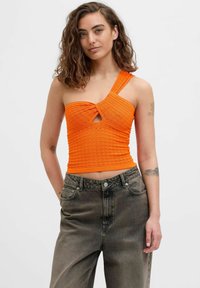 Top corto naranja con un diseño de canalé texturizado, detalle de ojal y una sola tirante en el hombro, combinado con unos jeans grises de talle alto.