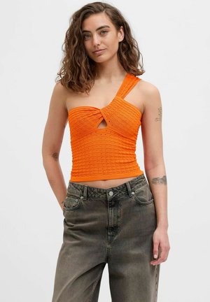 Crop top arancione con design a coste testurizzate, dettagli a chiave e una spallina singola, abbinato a jeans grigi a vita alta.
