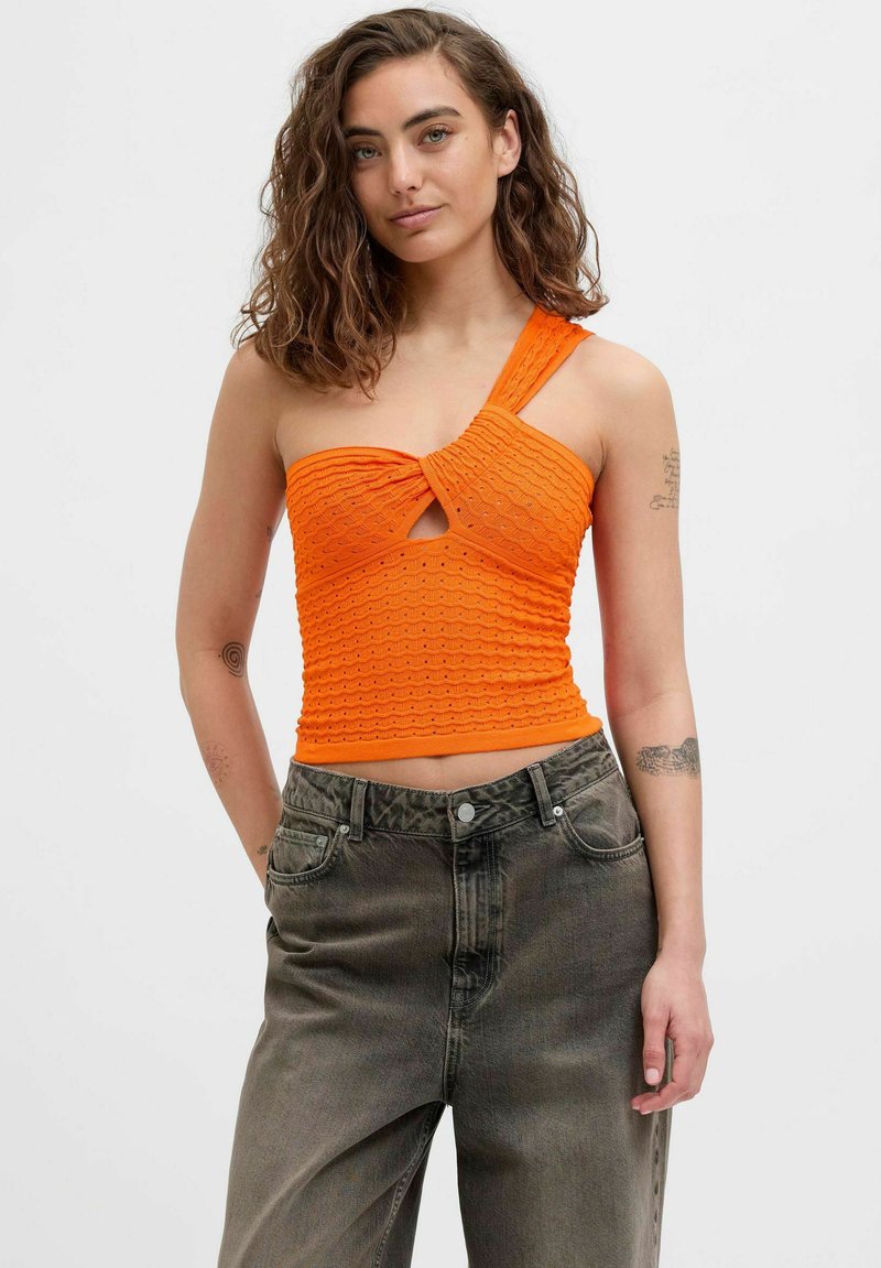 Top corto naranja con un diseño de canalé texturizado, detalle de ojal y una sola tirante en el hombro, combinado con unos jeans grises de talle alto.