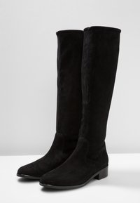 Bottes hautes jusqu'au genou en daim noir avec un bout arrondi, un talon plat à bloc et un design sans coutures. Texture lisse, détails de couture minimaux.
