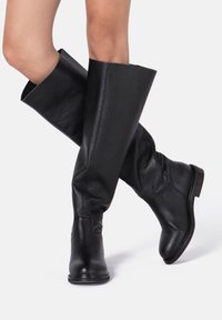 Bottes en cuir noir montant jusqu'au genou avec une finition texturée, un bout arrondi et un talon légèrement relevé, présentant un design supérieur souple pour un confort accru.
