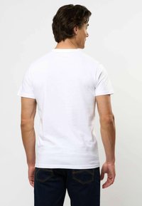 Biała koszulka z krótkim rękawem o okrągłym dekolcie, charakteryzująca się gładką fakturą i dopasowanym krojem. Noszona z ciemnoniebieskimi dżinsami.