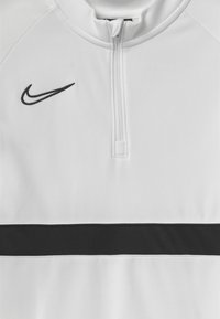 Weißer Halbreißpullover mit einem schwarzen horizontalen Streifen, der ein kleines schwarzes Nike-Logo auf der oberen linken Seite und einen glatten, strukturierten Stoff aufweist.