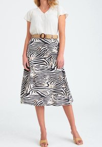 Kvinna klädd i en vit kortärmad blus, zebramönstrad midikjol med ett vävt tanbälte, och tanfärgade sandaler med öppen tå och klack.